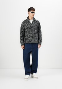 Fliisist pullover musta leopardi mustriga, hall värv, tõusva kraega, lukuga sulgemine, koos lahtiste siniste teksade ja valgete tossudega.