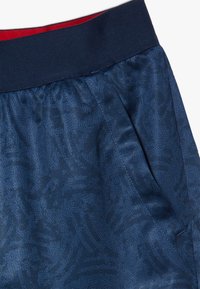 Marinblå shorts med ett texturerat mönster, elastisk midja med röda detaljer, sidofickor och ett mjukt, lätt tyg.