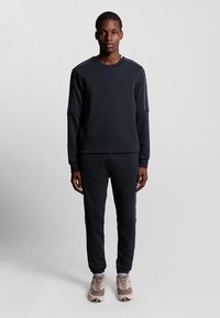 Felpa atletica grigio scuro e pantaloni abbinati con una vestibilità comoda, caratterizzati da cuciture a contrasto e caviglie rifinite. Indossati con sneaker chiare.