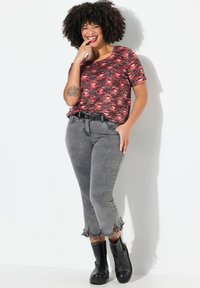 Camisa de manga corta con un patrón rojo y negro combinada con jeans grises con dobladillo deshilachado, llevada con botas de tobillo negras con detalles de tachuelas.