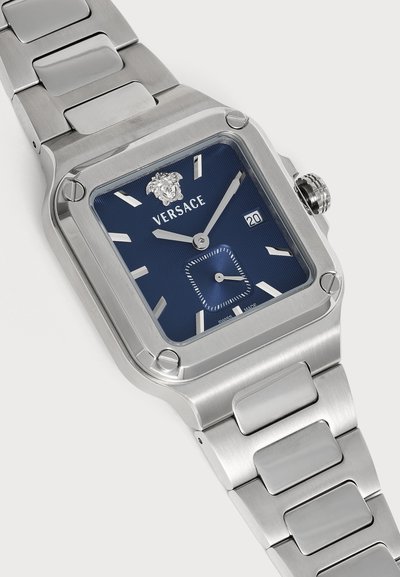 Montre-bracelet en métal argenté avec cadran carré bleu, index horaires argentés, afficheur de date et logo Versace avec la tête de Méduse à 12 heures.