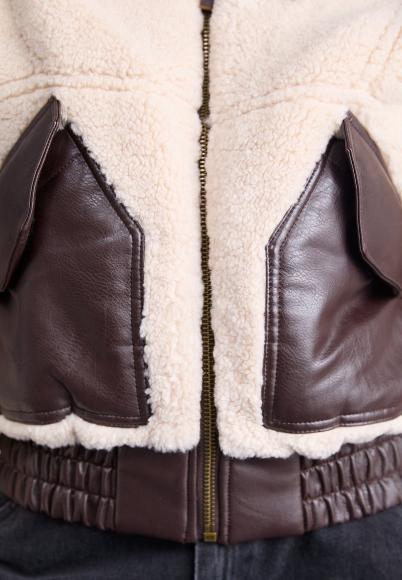 Braune Leder- und cremefarbene Sherpa-Jacke mit einem Reißverschluss vorne, geripptem Taillenbund und aufgesetzten Taschen mit glatten Akzenten.