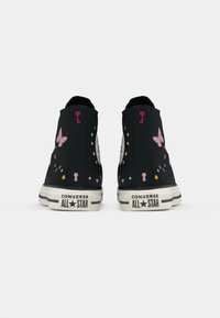 Mustad musta Converse tõuksi, millel on värvilised tikitud mustrid, sealhulgas liblikad, võtmed ja tähed kangast ülemise osa peal.