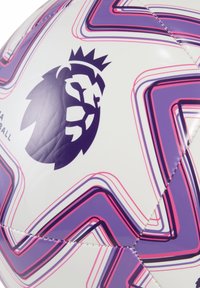 Biely futbalový lopt s fialovým logom leva, s tvary v podobe zúbkavých fialových a ružových čiar, šitými švami a lesklým povrchom.