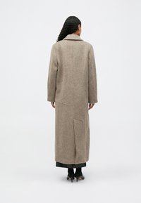 Długi, beżowy płaszcz wełniany z wykładanym kołnierzem, bocznymi kieszeniami i prostym krojem, z teksturowanym wykończeniem i długością poniżej kolan.
