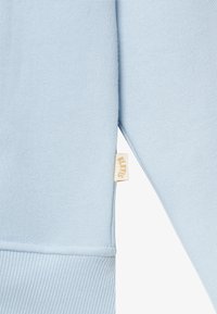 Helles blaues Sweatshirt aus weichem Stoff, mit einem gerippten Saum und Bündchen, und einem kleinen beigen Etikett, das an der Seite angenäht ist.