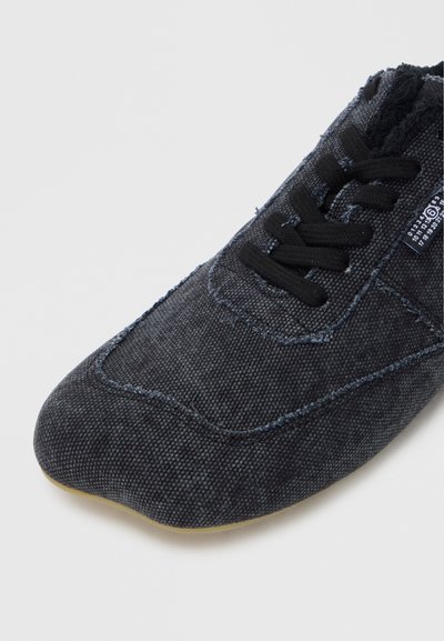 Σκούρο γκρι υφασμάτινο παπούτσι με λεία επιφάνεια, στρογγυλεμένη μύτη, μαύρα κορδ�όνια και διακριτικές ραφές. Διαθέτει ευέλικτη σόλα.