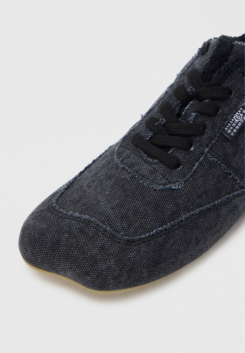 Mørkegrå tekstilsko med en glat overflade, rundet tå, sorte snørebånd og diskrete syningsdetaljer. Har en fleksibel sål.