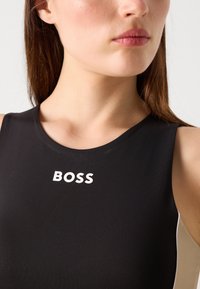Top atletico nero con collo rotondo e logo BOSS bianco. Presenta un design aderente e dettagli di colore in contrasto sui lati.