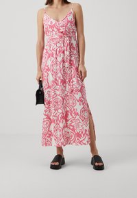 Sukienka maxi na cienkich ramiączkach, różowo-biały kwiatowy wzór, marszczona talia, rozcięcie z boku, w połączeniu z czarnymi sandałami na platformie.