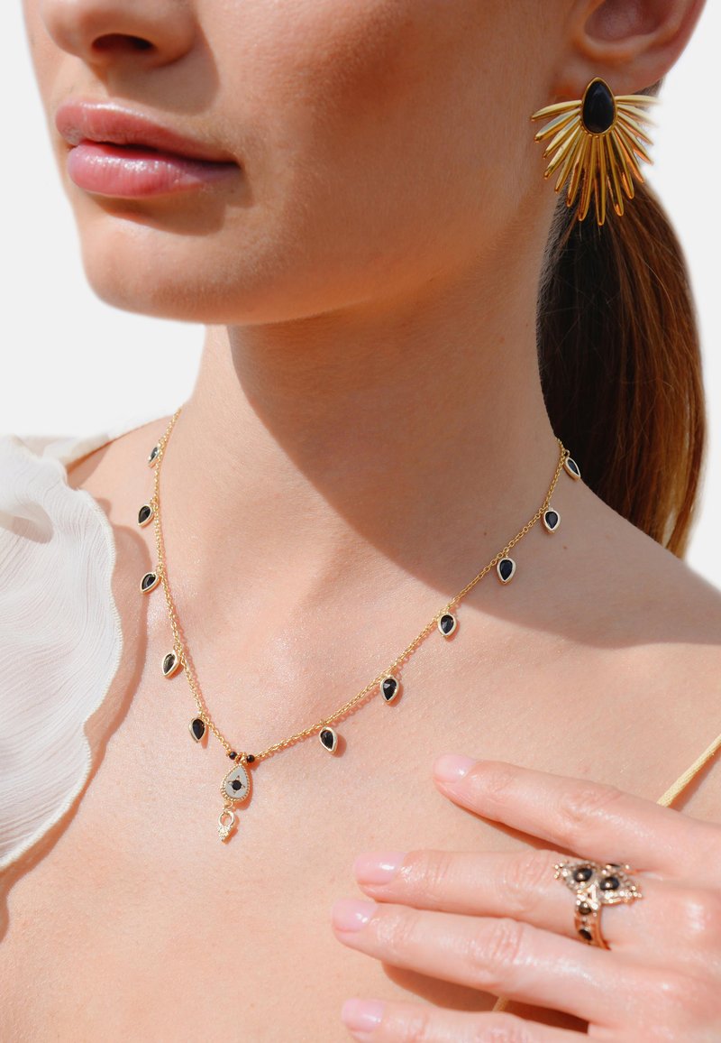 Collier en or avec des pierres noires en forme de goutte, arborant un pendentif central. Boucles d'oreilles en or avec une pierre noire et un design en rayons de soleil.