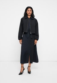 Jachetă neagră scurtă cu guler, purtată peste o rochie lungă cu imprimeu leopardo în nuanțe închise, având talie legată și fante în față, asortată cu tocuri negre.