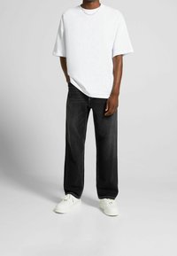 T-shirt bianca oversize, pantaloni in denim neri e sneakers bianche. Presenta maniche corte e una vestibilità rilassata. Design semplice e classico.