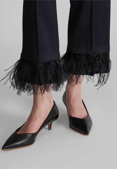 Scarpe nere con tacco alto e punta affusolata, abbinate a pantaloni blu con un bordo piumato all'orlo. Dettagli in piuma testurizzati alla caviglia.
