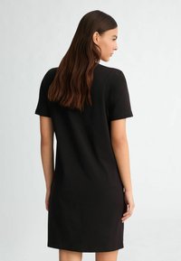 Rochie neagră cu mânecă scurtă, cu o siluetă dreaptă, fabricată dintr-un material neted, având un design minimalistic și fără modele vizibile.