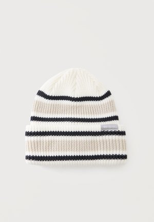 Dziergana czapka typu beanie z białymi, beżowymi i czarnymi poziomymi paskami oraz podwiniętym mankietem na jasnym tle.