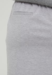Pantaloni sport gri, cu un material texturat, talie elastică și un detaliu mic în formă de buzunar orizontal pe spate.