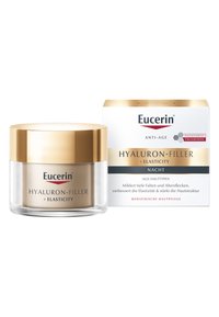 Eucerin Hyaluron-Filler + Elasticity Nachtcreme in einem runden Glasbehälter mit einem goldenen Deckel, begleitet von einer weißen und goldenen Box, enthält Anti-Aging-Eigenschaften.