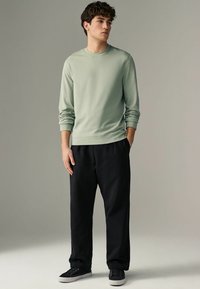 Sudadera de manga larga verde claro con cuello redondo, combinada con pantalones de chándal negros holgados y zapatillas negras con suelas blancas.