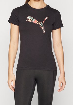 Kobieta nosząca czarną dopasowaną koszulkę z wielokolorowym kwiatowym logo Puma na piersi i czarne legginsy.