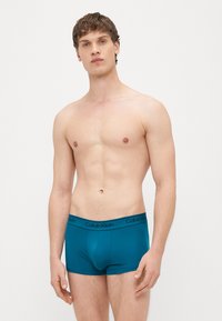 Tirkīza krāsas kokvilnas bokseršorti ar melnu Calvin Klein logotipu uz jostasvietas, rādot pieguļošu dizainu un gludu tekstūru.