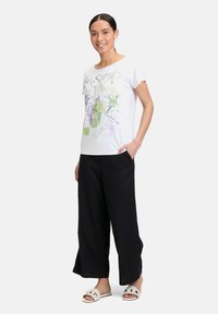 Biała koszulka z krótkim rękawem z kolorową grafiką lemoniady i napisem. W połączeniu z czarnymi spodniami o szerokich nogawkach i jasnymi sandałami.