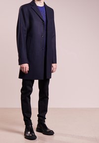 Manteau en laine marine avec trois boutons et une poche poitrine simple, associé à un pantalon noir ajusté et des bottes Chelsea noires brillantes.