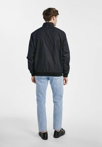 Czarna, lekka kurtka z stójką, elastycznym dołem i mankietami. Nosi się ją na jasnoniebieskie dżinsy i czarne buty. Prosty design, bez wzorów.