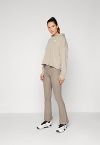Sudadera corta beige con logo, combinada con pantalones acampanados ajustados de tejido suave a juego. La modelo lleva zapatillas deportivas en blanco y negro.