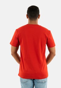 Camiseta de algodón roja de mangas cortas con cuello redondo. Presenta un diseño limpio y un corte regular, mostrada desde la parte de atrás.