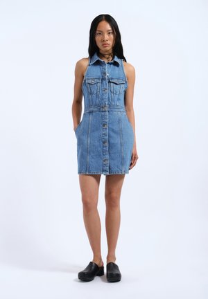 Denim dress with a fitted silhouette, light blue color, button front, collar, chest pockets, and side pockets. Worn with black clogs.