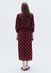 Burgunderfarbiges Midikleid mit weißen Punkten, das eine taillierte Taille und Ballonärmel aufweist, aus leichtem Stoff gefertigt. Getragen mit schwarzen Sandalen.