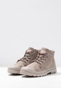 Botas altas de ante beige con acentos en rosa, puntera redondeada, parte delantera con cordones y suela de goma texturizada. Presenta un logotipo en el costado.