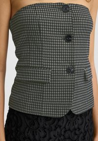 Melnbalta houndstooth bezsānu topa ar divām melnām pogām un sānu kabatām, ar pieguļošu dizainu un gludu tekstūru.