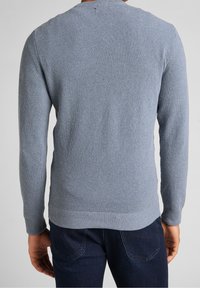 Ljusblå stickad tröja med ett strukturerat mönster, rund halsringning och ribbade muddarna och nederkant, bärs över mörka denimjeans.