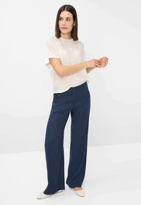 T-shirt chiaro color crema con maniche corte abbinato a pantaloni ampi blu navy, dotati di chiusura a bottoni e tessuto testurizzato.
