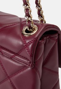 Bolso de mano de cuero burdeos con un diseño acolchado, detalles en hardware dorado y una correa de cadena trenzada, con costuras visibles.