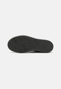 Semelle de chaussure en caoutchouc noir avec un motif texturé en points. La marque "Camper" est imprimée à divers endroits sur la surface.