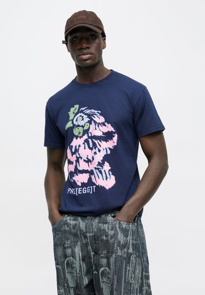 Μπλουζάκι από βαμβάκι σε ναυτικό μπλε με πολύχρωμο γραφικό σχέδιο σε ροζ, πράσινους και μπλε τόνους, σε συνδυασμό με σκουρόχρωμο παντελόνι με σχέδια.