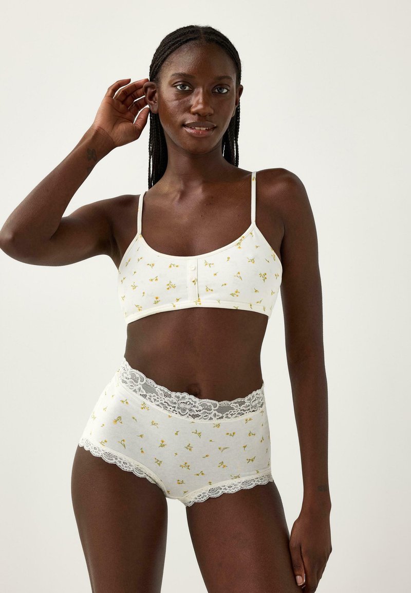 Bralette in cotone bianco con stampa floreale gialla, dotato di bottoni frontalmente e spalline sottili, abbinato a slip a vita alta con pizzo.