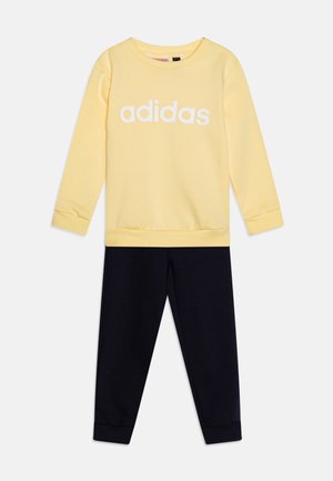 Sudadera amarilla con el logo blanco de "adidas", complementada por pantalones de cintura elástica en azul marino oscuro. Tejido suave, mangas largas y puños acanalados.