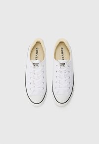 Hvite lerrets-sneakers med lav topp, svart gummisåle og klassisk snøring foran. Har et logo-stempel på tungen.
