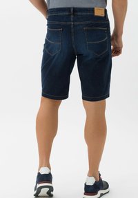 Tummansiniset denimit hameet suoran leikkauksen omaavina, joissa on kaksi taustataskua, joita korostaa keltainen tikkaus. Ne on yhdistetty tummiin urheilukenkiin.