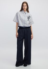 Camicia a maniche corte a righe in bianco e blu navy con un dettaglio grafico, abbinata a pantaloni larghi blu navy con vita arricciata.