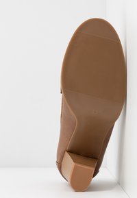 Chaussure marron à talon positionnée semelle vers le haut, montrant la semelle extérieure texturée et le talon bloc avec la taille 39 indiquée sur la semelle.