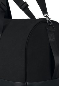 Černý sportovní vak s hladkým textilním tělem, strukturálním kulatým tvarem, polstrovaným ramenním popruhem a koženými akcenty na dně.