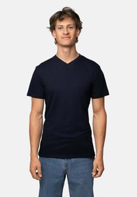 Camiseta de algodón azul marino con un diseño de cuello en V. Mangas cortas y una forma ajustada. Combinada con jeans de mezclilla casual de color azul claro.