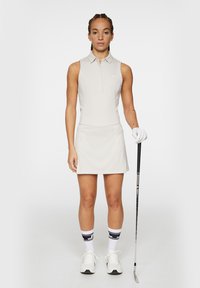 Ljus beige ärmlös golfklänning med krage och smal passform, med ett midjeband, kombinerad med vita skor och strumpor med svarta accenter.