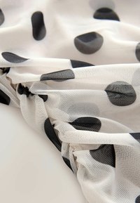 Gennemsigtig stof med sorte prikker på en cremefarvet baggrund, med en samlet tekstur og et let, netlignende udseende.