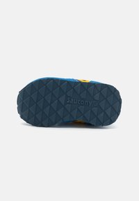 Blå og gul sneaker med en teksturert gummisåle som har et geometrisk mønster og en preget "Saucony"-logo.